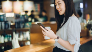 Young woman using smartphone while having her cup of coffee and taking a break in a coffee shop