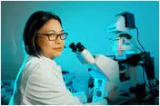 WHite lab coated scientist looks sceptical in front of microscope. Photo by Shutterstock